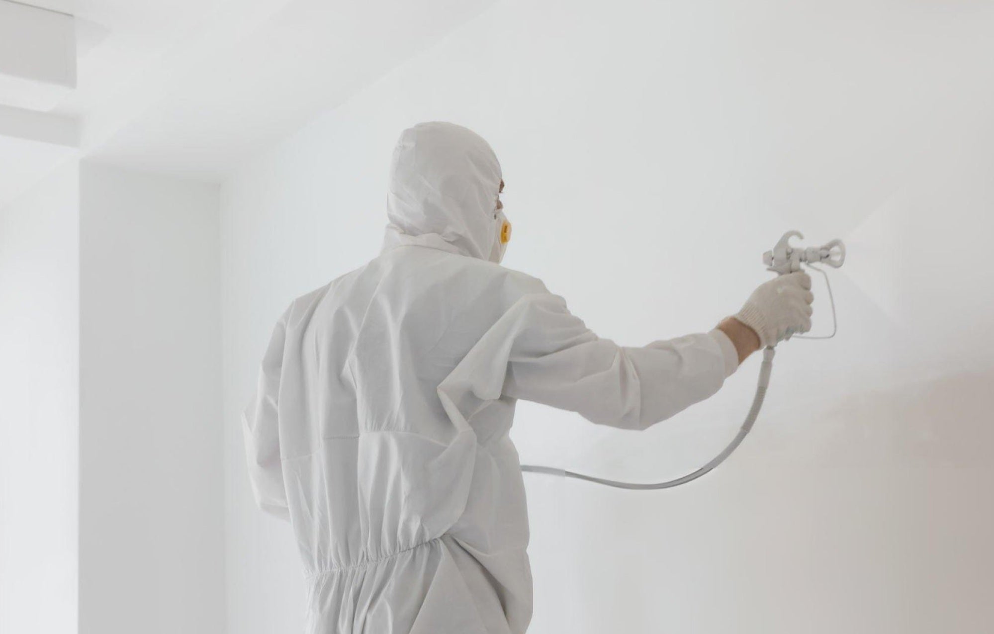 Clean living room prepped for spraying with masked trim, covered furniture, and an HVLP sprayer ready to use