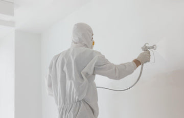 Clean living room prepped for spraying with masked trim, covered furniture, and an HVLP sprayer ready to use