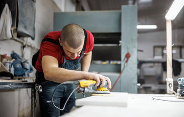 Professional technician using a random orbital sander with dust extraction in a workshop, clean lighting and safe PPE