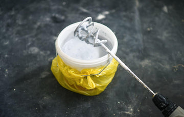 Professional using a drill with a paddle mixer attachment to mix paint or mortar in a bucket with dust-safe PPE, clean workshop background