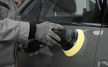 Professional technician using a machine polisher on car door panel for paint correction